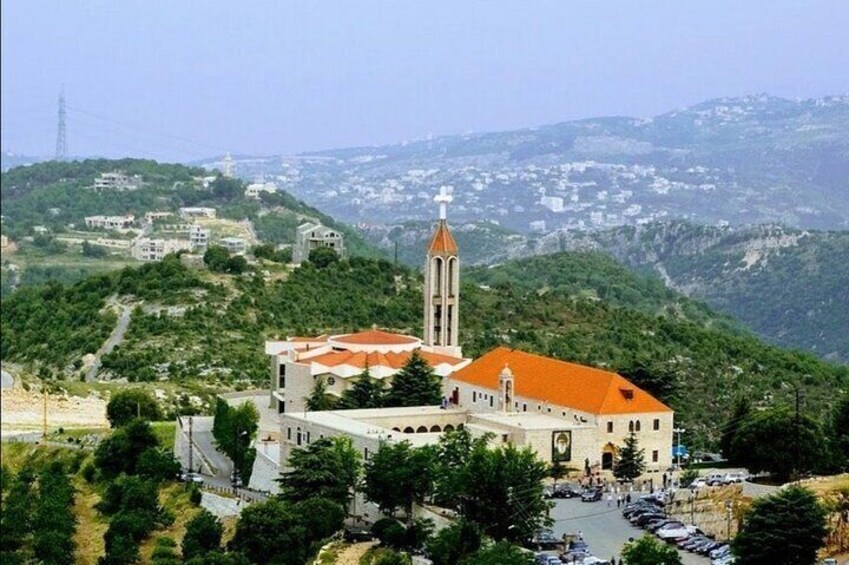 A church with a tall bell tower and red roof, surrounded by greenery and hills. 2