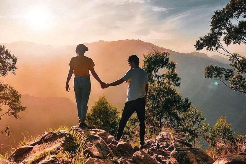 Dos personas tomadas de la mano en un afloramiento rocoso, con un paisaje montañoso al fondo. 3