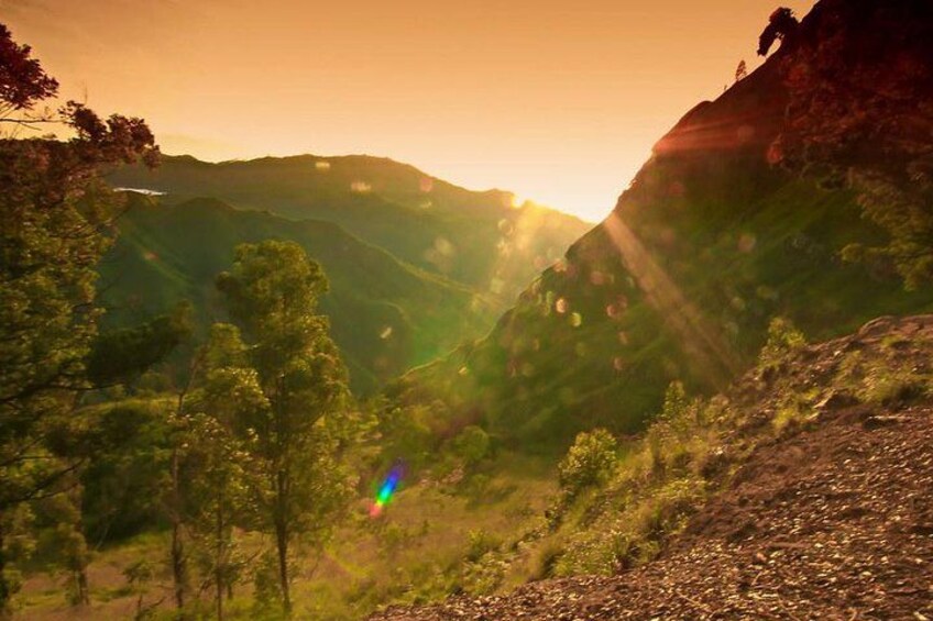 A mountainous landscape with a valley, trees, and sunlight filtering through. 4