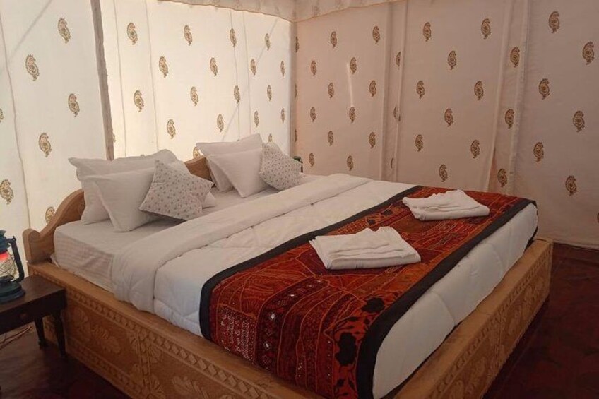 Een bed met witte lakens en een rood geborduurde plaid, een houten hoofdbord en behang met een patroon. 2