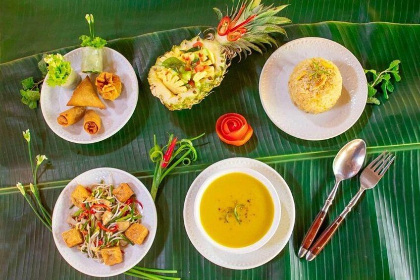 A variety of dishes on a banana leaf, including a bowl of soup, a plate of fried items, and a dish with a pineapple centerpiece. 2