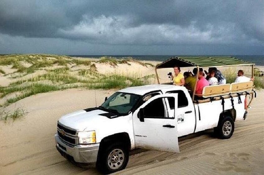 Een witte pickup truck geparkeerd op een zandstrand, met duinen op de achtergrond. 2