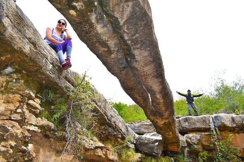 Eine Person sitzt auf einer Felsstufe, eine andere Person steht auf einem Felsen, und im Hintergrund steht ein großer Baum. 4