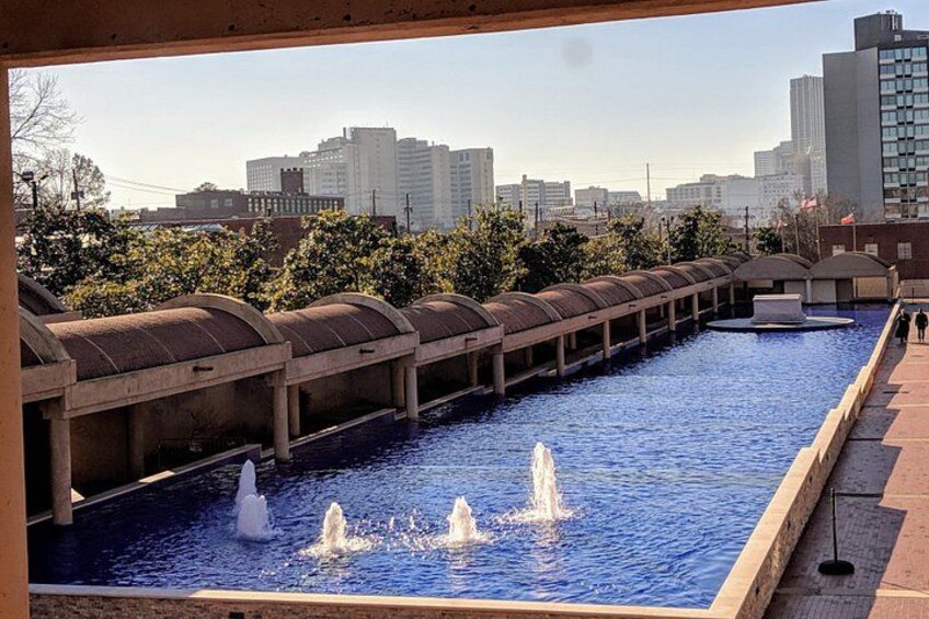 A water feature with multiple fountains, a metal structure, and a cityscape in the background. 2