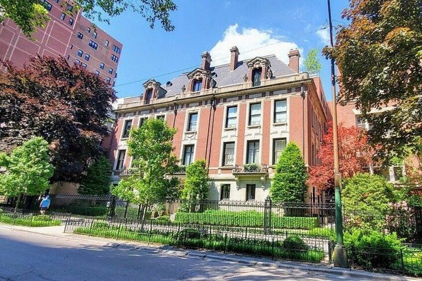 Un bâtiment en briques rouges, avec une clôture verte et des arbres devant. 2