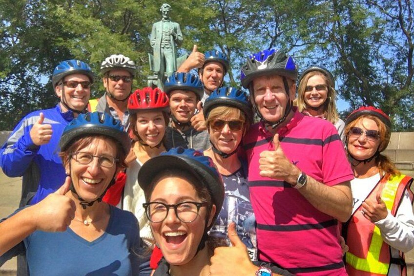 Un groupe de personnes portant des casques et des vêtements de cyclisme, posant pour une photo devant une statue. 3
