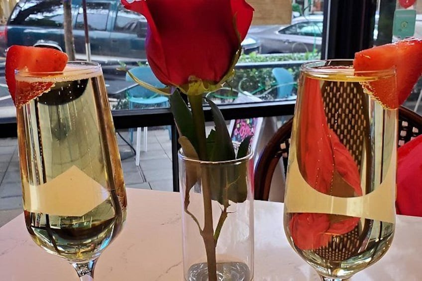 Two glasses of white wine with rose petals and a red rose in a vase. 3