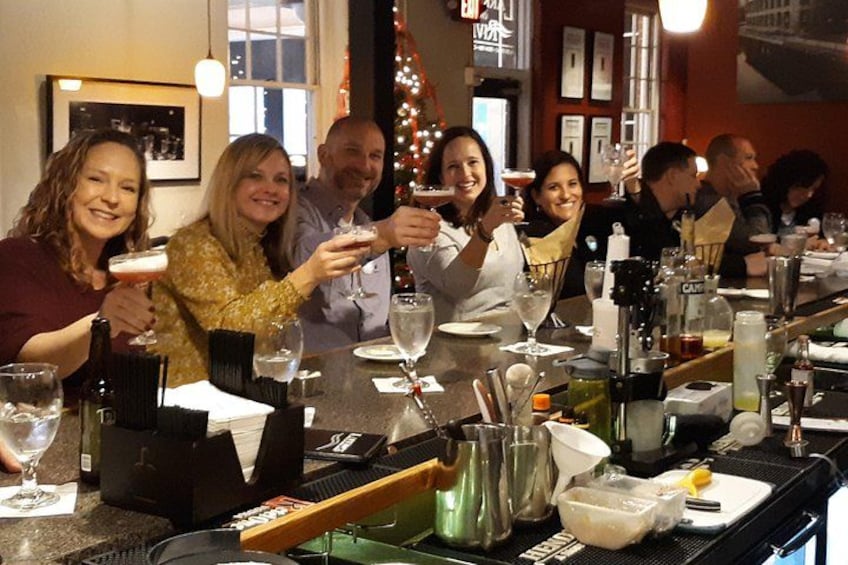 A group of people toasting at a bar with various bottles and glasses. 4