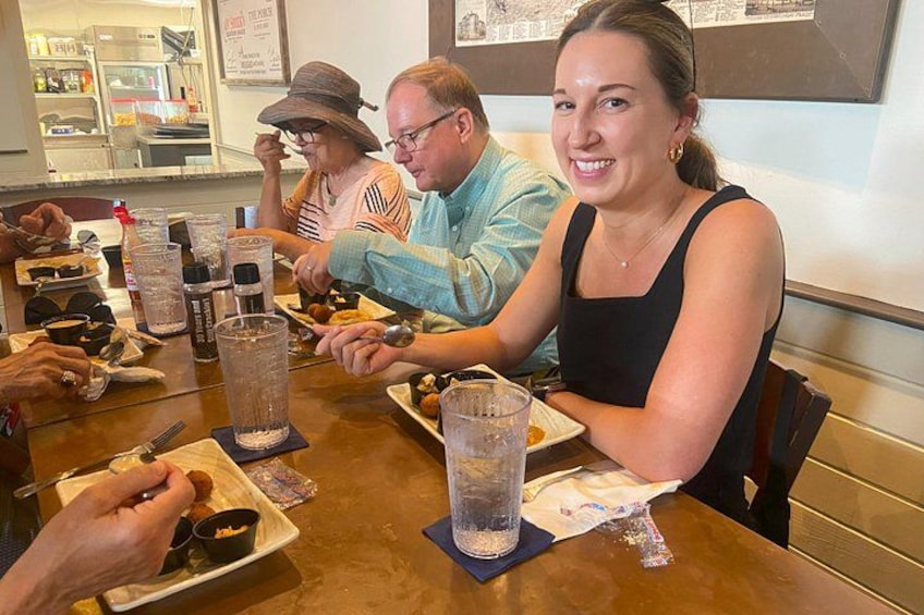 Un grupo de personas cenando en un restaurante, con platos de comida, bebidas y salsas sobre la mesa. 2