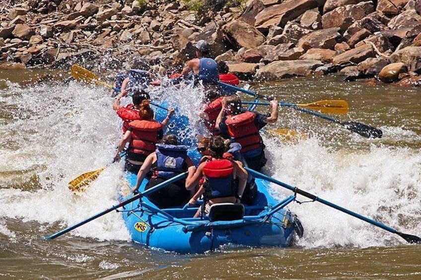 A group of people in a blue raft navigating through a river with rapids. 1