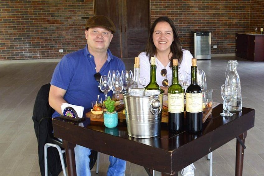 Twee personen zitten aan tafel met wijnflessen en glazen. 2