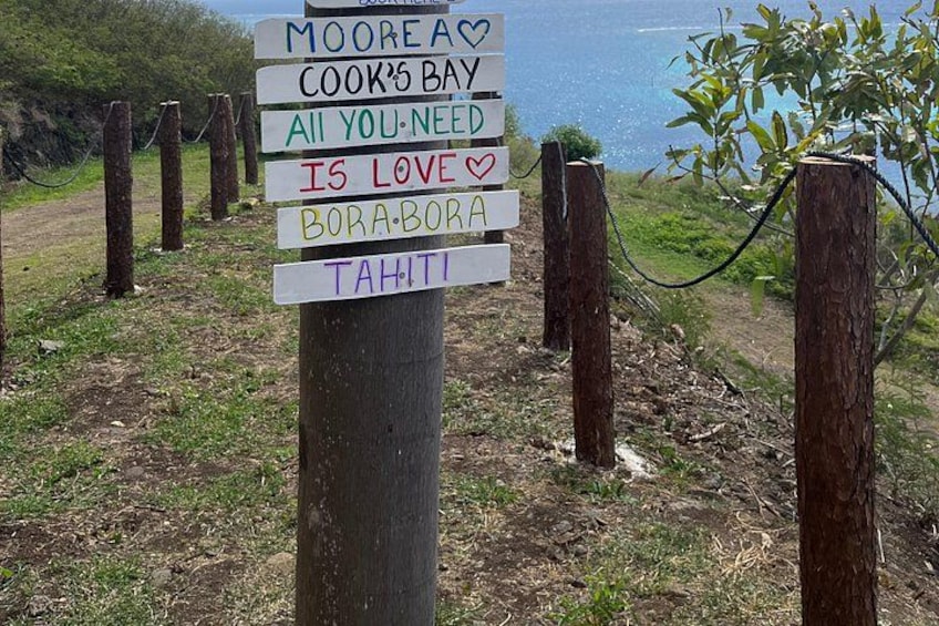 Un cartel con múltiples indicaciones, incluyendo 'MOOREA', 'COOKE’S BAY', 'TODO LO QUE NECESITAS ES AMOR', 'BORA BORA' y 'TAHITI'. 3
