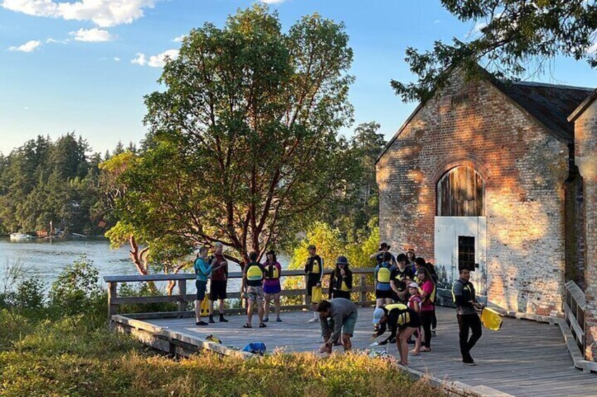 A group of people on a wooden dock near a brick building by a lake. 5