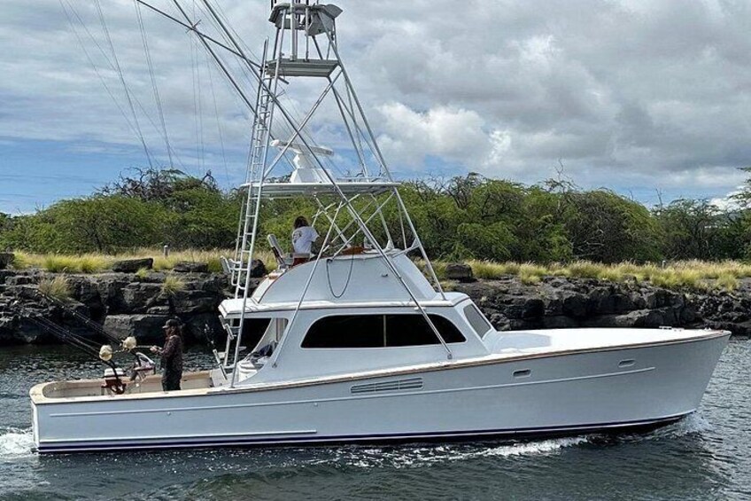 Un yacht blanc doté d’une cabine, avec une personne debout à la proue, naviguant sur des eaux calmes, avec une côte rocheuse et une végétation luxuriante en arrière-plan. 4