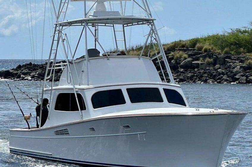 Un bateau blanc, doté d’une cabine et de cannes à pêche sur le pont, est amarré près d’une côte rocheuse. 2