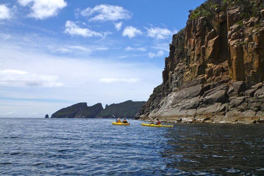 A kayaker on a calm sea, a rocky cliff, and a clear sky. 3
