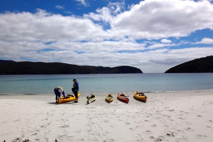 A beach with kayaks and a person preparing a kayak. 2
