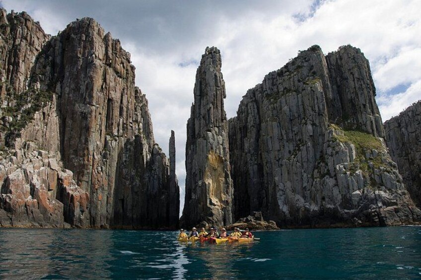 A group of people kayaking in a narrow waterway between tall, rocky cliffs. 1