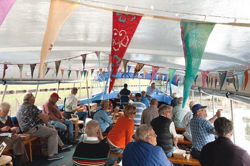 People seated in a covered area with colorful flags, tables, and chairs. 2