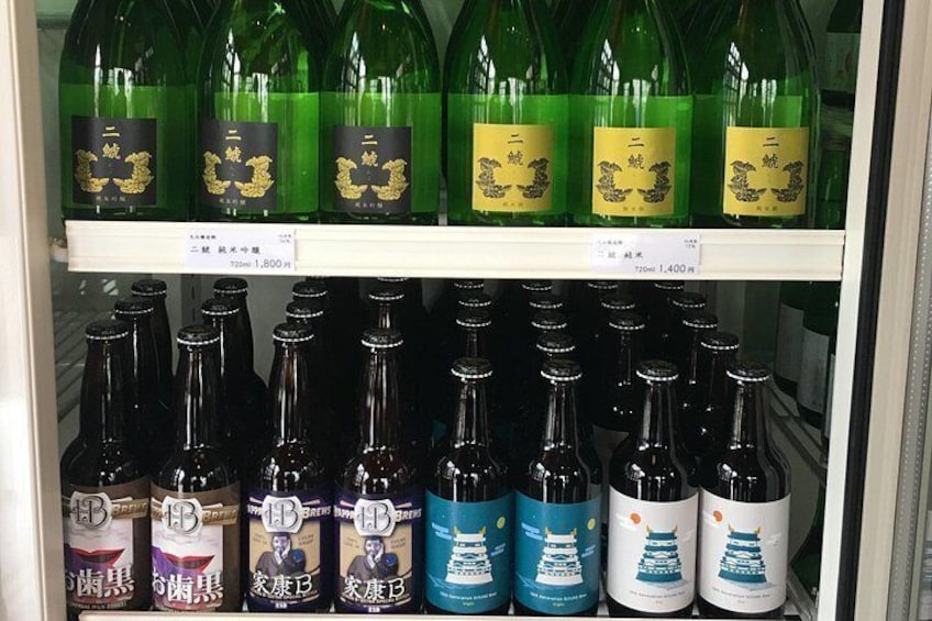 Un expositor refrigerado con diversas botellas de bebidas, algunas con etiquetas doradas y negras, y otras con etiquetas azules y blancas. 2