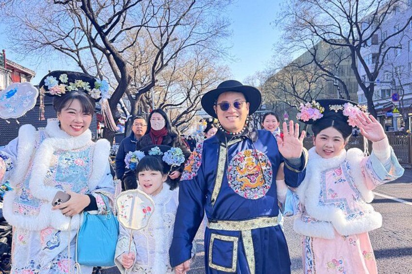 People in traditional costumes, a street with trees, and buildings in the background. 2