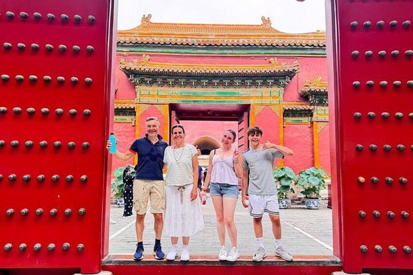 A group of people standing in front of a red gate with a traditional Chinese architectural structure in the background. 2