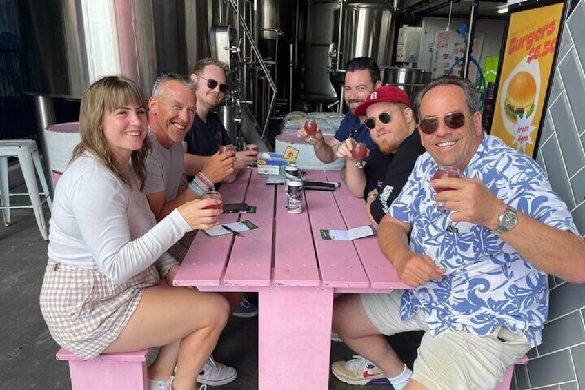 A group of people sitting at a pink table outdoors, possibly at a restaurant or food truck. 1