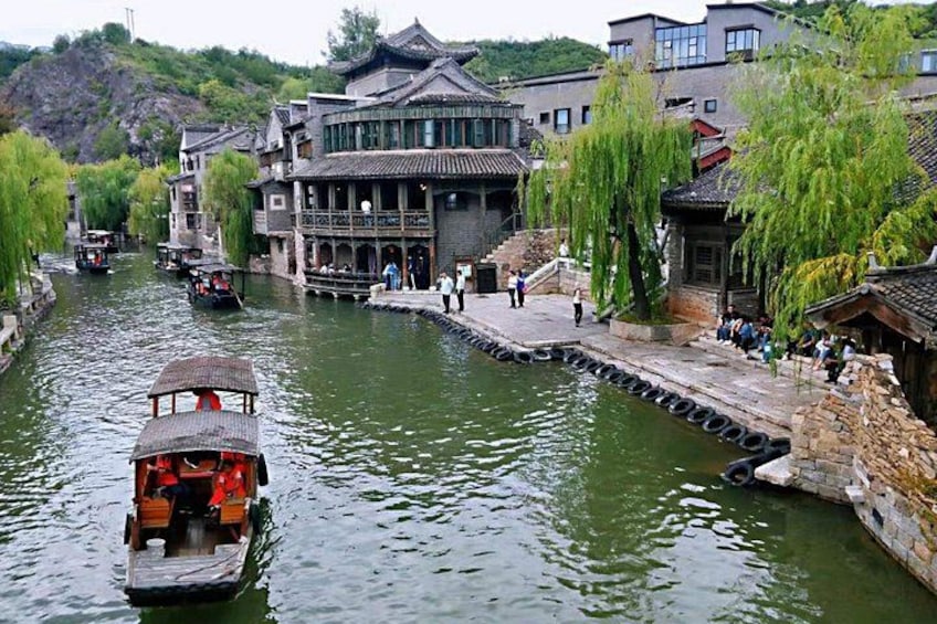 A traditional wooden boat on a river, traditional buildings, and people walking along the riverbank. 2