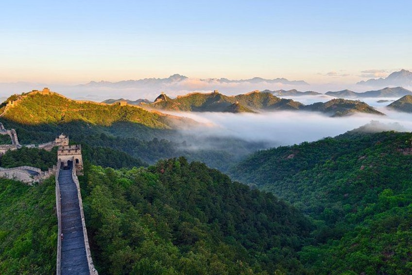 The Great Wall of China winding through lush green hills, with mist-covered mountains in the background. 3