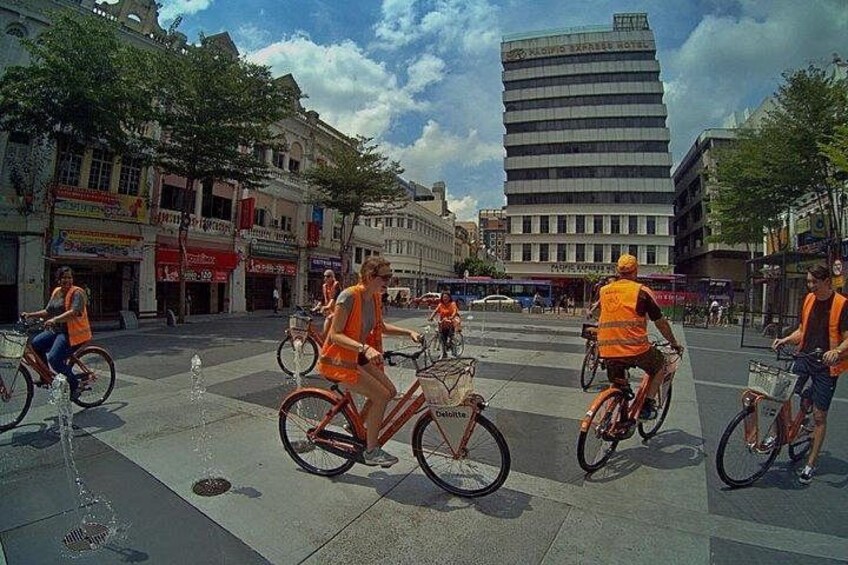 Een groep fietsers in oranje hesjes rijdt over een stadsstraat. 2