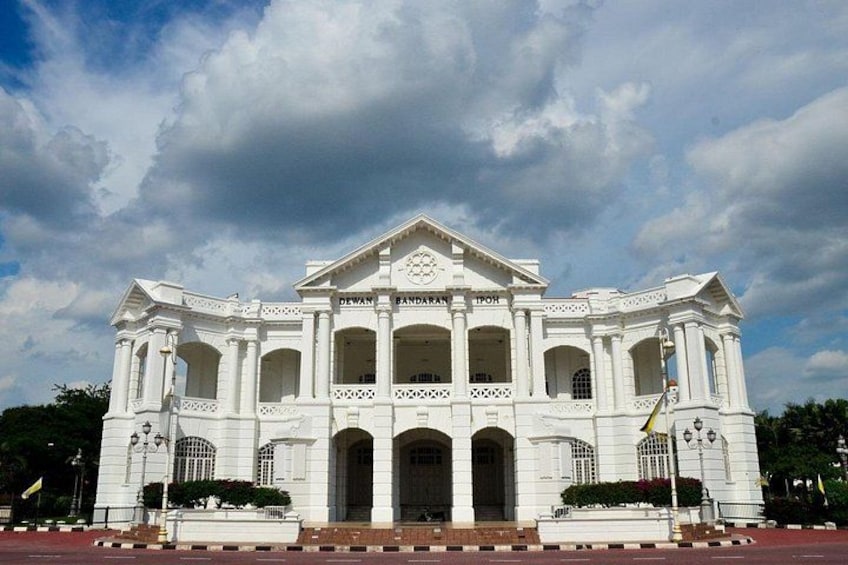 A white colonial-style building with multiple arches and columns, surrounded by a red pavement and greenery. 3