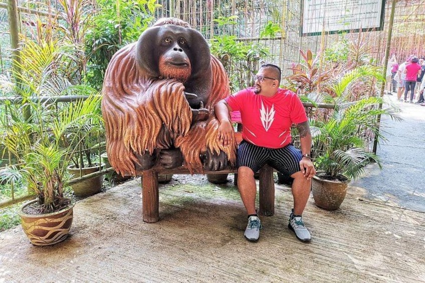 A person sitting on a bench next to a large orangutan statue in a garden with potted plants. 4