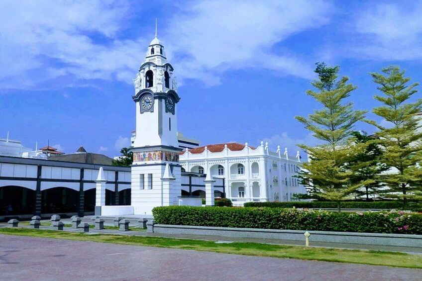 A white building with a clock tower, surrounded by greenery and a clear sky. 1