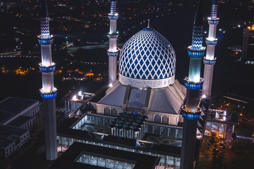 Een moskee met een grote koepel en vier minaretten, omgeven door een stadsgezicht in de nacht. 5
