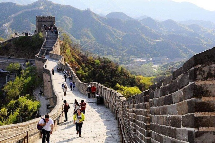 La Gran Muralla China serpenteando a través de un paisaje montañoso, con visitantes caminando por el sendero. 4