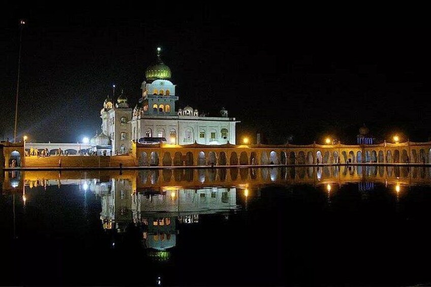 A night-time view of a well-lit historical building with a dome, surrounded by a reflective water body and a series of arches. 3