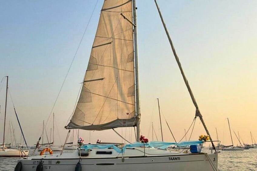 Ein Segelboot mit großem Segel, namens 'TAANTI', auf ruhigem Wasser. Im Hintergrund sind weitere Boote zu sehen. 1