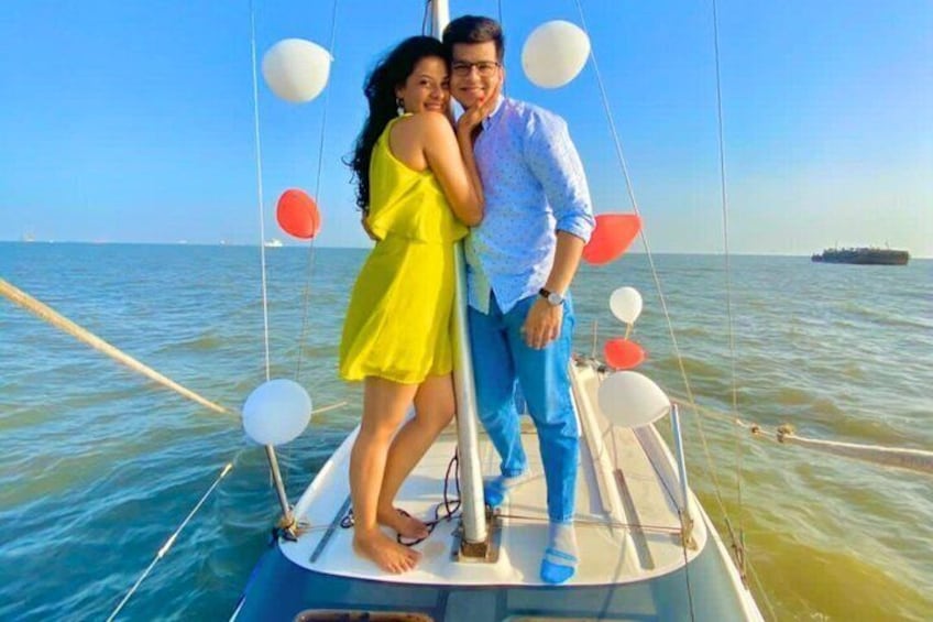 A couple on a sailboat with balloons and a ship in the background. 3