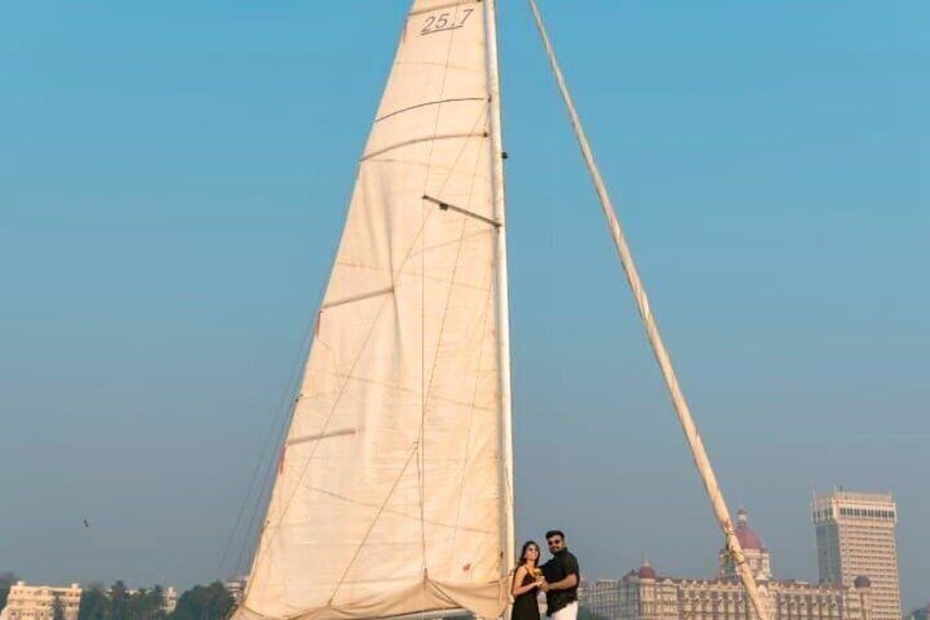 A sailboat with a large sail and a tall mast, with a cityscape in the background. 2