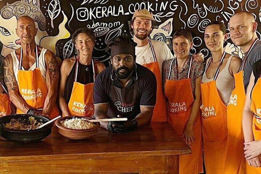Un groupe de personnes portant des tabliers orange sur lesquels on peut lire « CUISINE DU KERALA », et qui se tiennent devant un mur orné d’illustrations sur le thème de la cuisine. 2