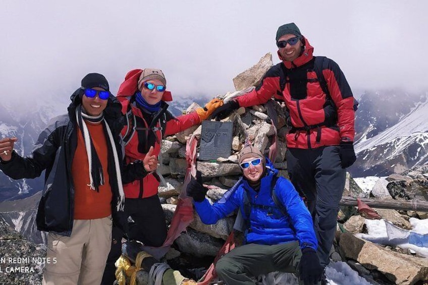 Four people on a mountain peak with snow-covered mountains in the background. 1