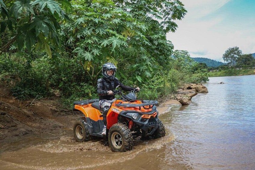 A person on an orange ATV navigating through a muddy riverbank. 5