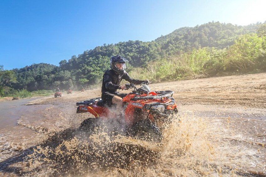 A person riding an ATV through a muddy area with splashes of water. 3