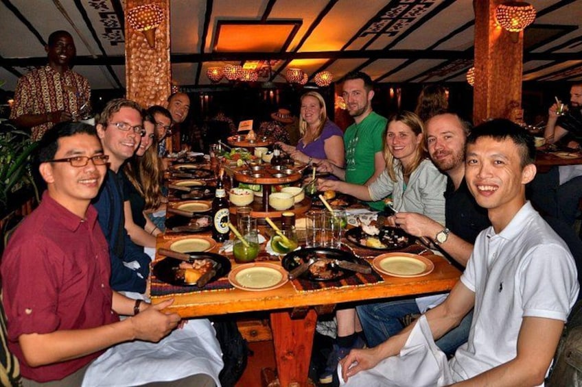 Un groupe de personnes est assis autour d’une longue table en bois, devant divers plats et boissons. 1