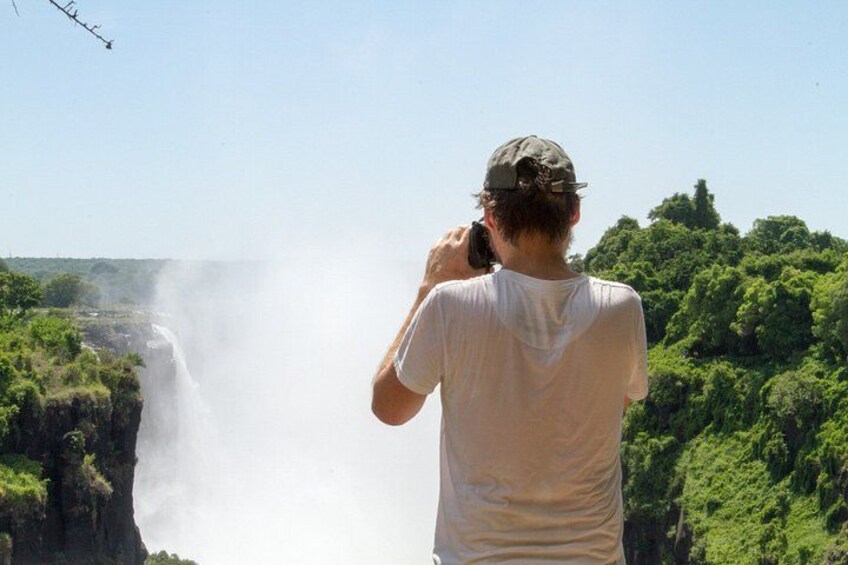 A person taking a photo of a waterfall with lush greenery in the background. 2