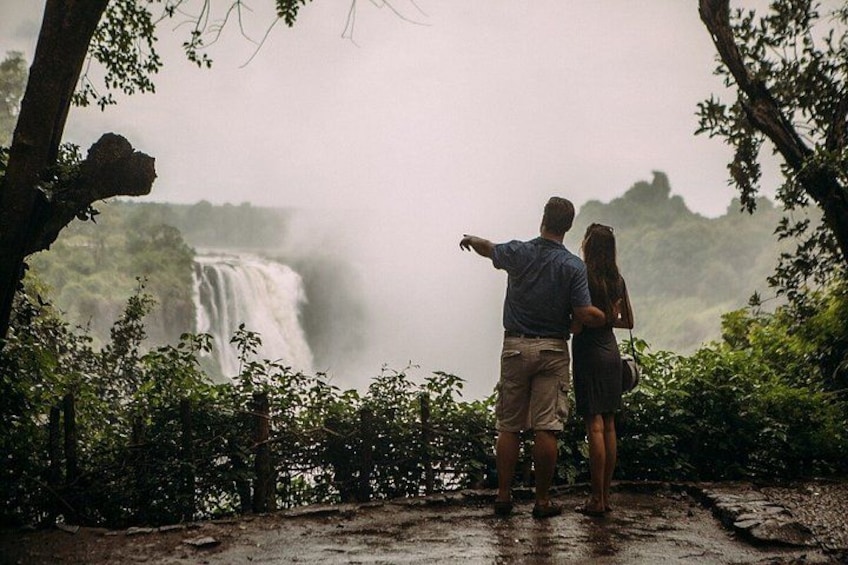 A couple standing on a path, overlooking a waterfall surrounded by dense foliage. 3