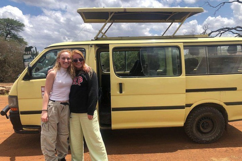 A yellow van with a roof rack, parked on a dirt road with trees in the background. 1