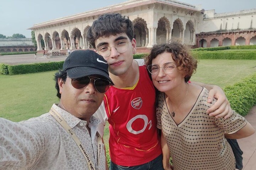 Una persona con una camisa estampada tomándose un selfie con otras dos personas frente a un edificio histórico con arcos. 5