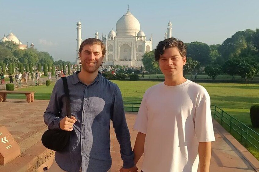 Dos personas frente al Taj Mahal, con vista despejada al monumento y la vegetación circundante. 4