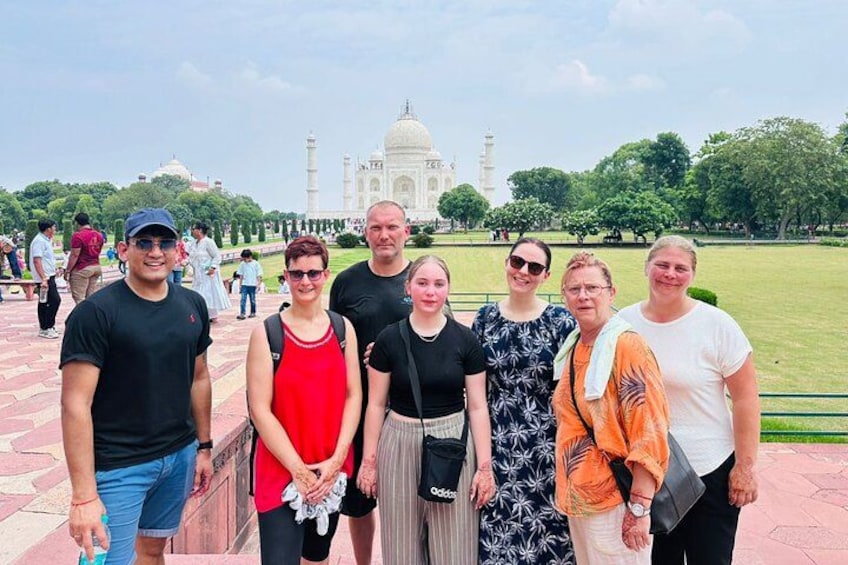 Un grupo de personas frente al Taj Mahal, con un amplio césped y árboles al fondo. 1